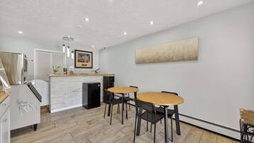 A modern kitchen with a white countertop, a built-in refrigerator, and a dining area with wooden tables and black chairs.