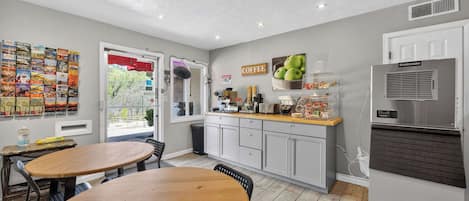 A compact kitchen with a refrigerator, a coffee station, and a dining area with two wooden tables.