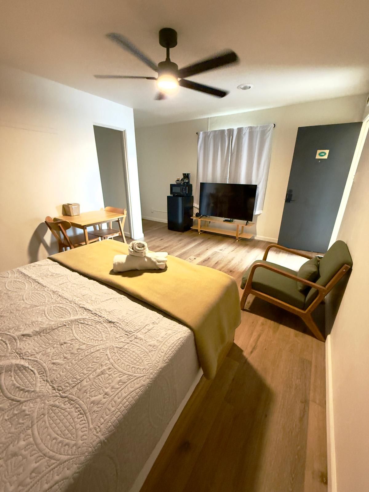 A hotel room with two beds, a TV, a ceiling fan, a small table with a chair, and a window with curtains.