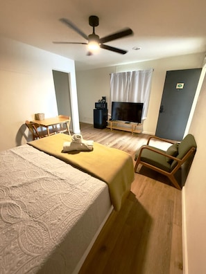 Ein Hotelzimmer mit zwei Betten, einem Fernseher, einem Deckenventilator, einem kleinen Tisch mit Stuhl und einem Fenster mit Vorhängen.