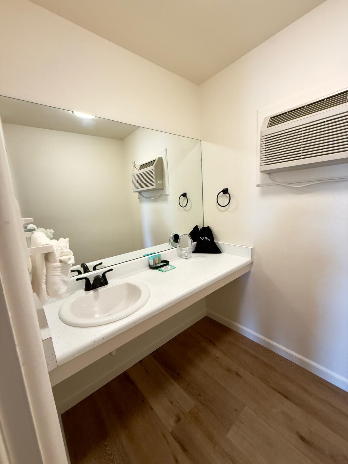 A bathroom with a white sink, mirror, and towel rack. There is a white air conditioning unit on the wall.