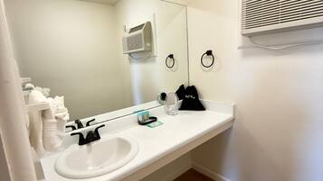 A bathroom with a white sink, mirror, and towel rack. There is a white air conditioning unit on the wall.