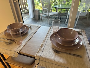 A table set with brown plates, a glass, and cutlery, with a view of outdoor furniture and greenery through a glass door.