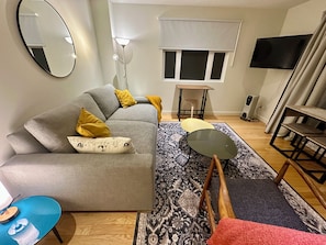 A modern living room with a grey sofa, a small round table, a patterned rug, and a television on the wall.