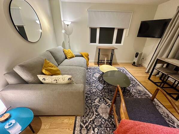 A modern living room with a grey sofa, a small round table, a patterned rug, and a television on the wall.