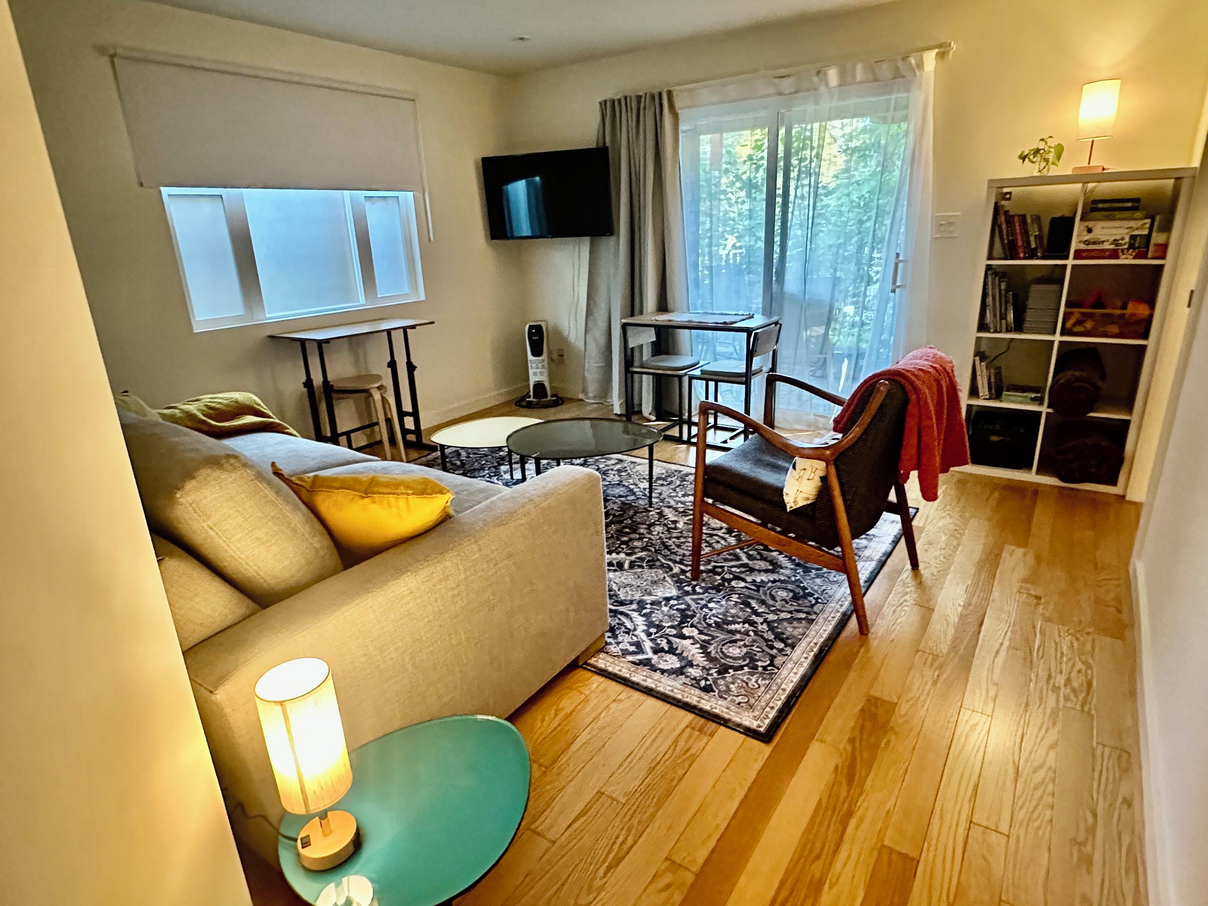 Ein Wohnzimmer mit einer Couch, einem Couchtisch, einem an der Wand montierten Fernseher, einem Bücherregal und einem Fenster mit Vorhängen.
