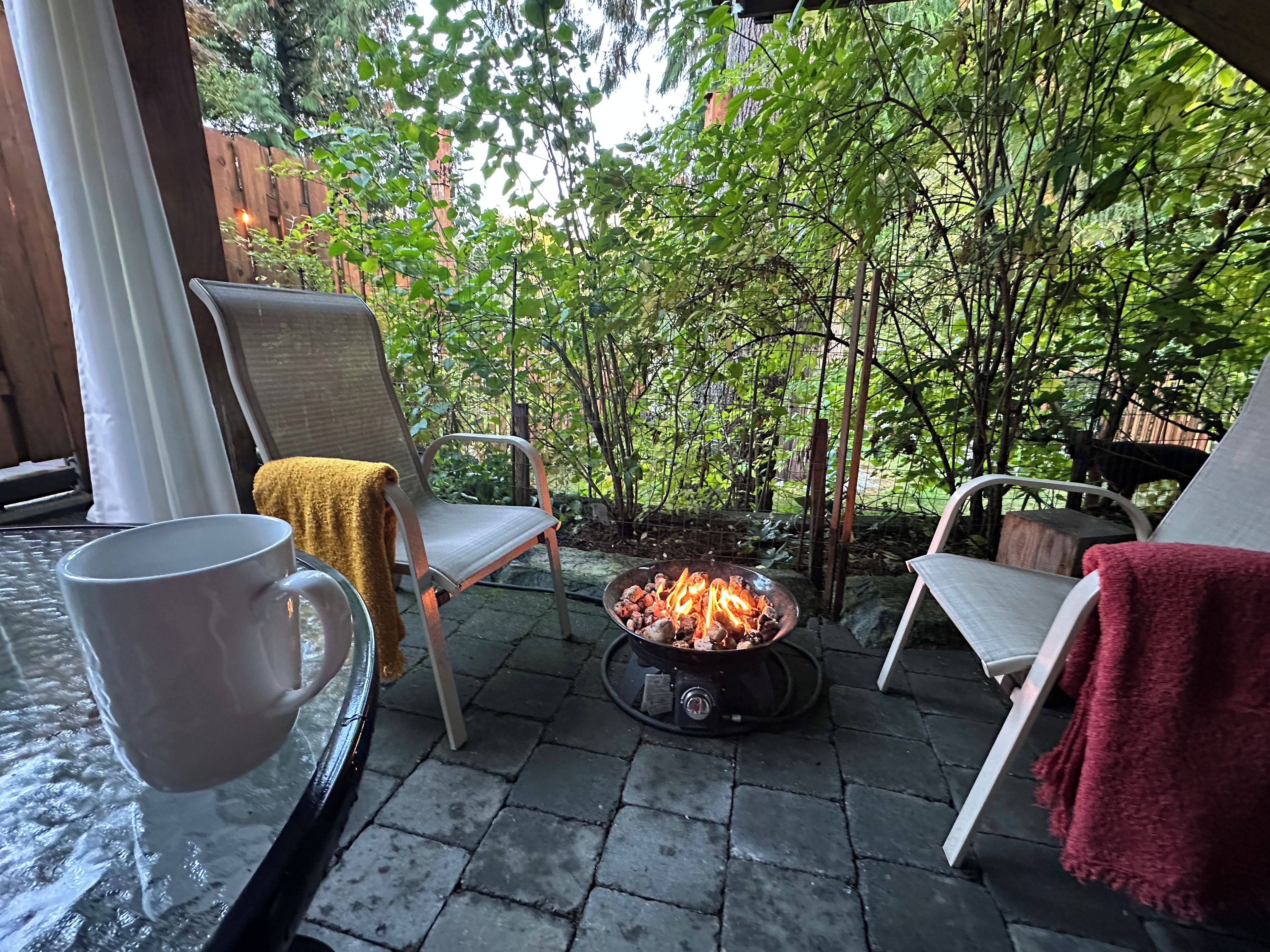 Eine Terrasse mit Feuerstelle, zwei Stühlen und einem Tisch mit einer Tasse.