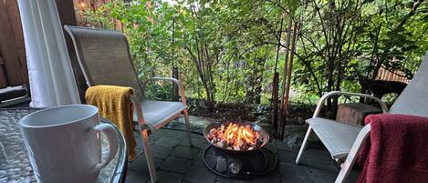 A patio with a fire pit, two chairs, and a table with a mug.