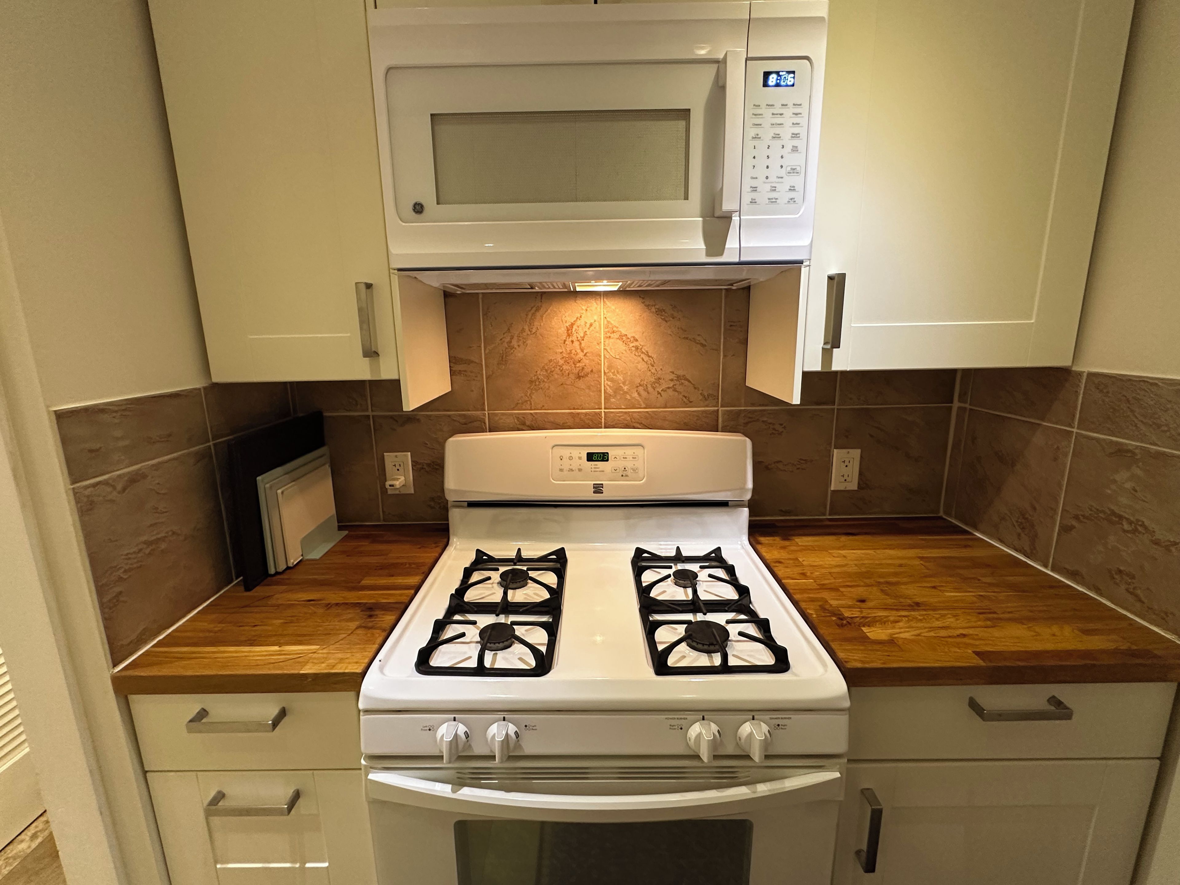 A kitchen with a gas stove, oven, microwave, and wooden countertop.