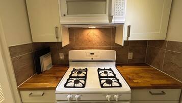 A kitchen with a gas stove, oven, microwave, and wooden countertop.