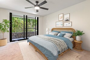Ein Schlafzimmer mit einem Bett, einem Deckenventilator, einem Fenster mit Blick auf Grünflächen und gerahmten Bildern an der Wand.