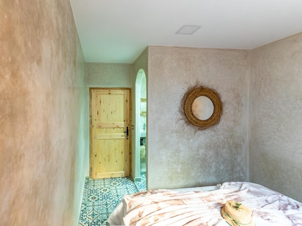 A bedroom with a bed, a wooden door, and a wall-mounted mirror.