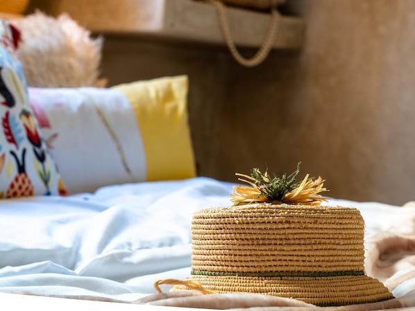 A bed with a woven basket on it, a colorful pillow, and a beige bag hanging on the wall.