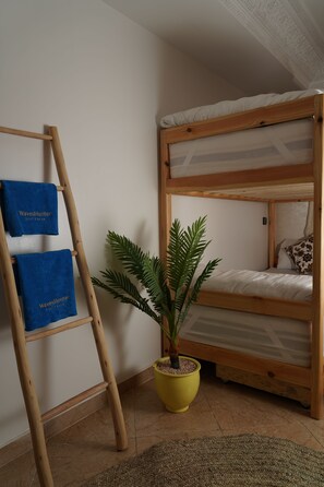 A bunk bed with a wooden frame and white bedding, a wooden ladder, two blue towels with text, and a potted plant.