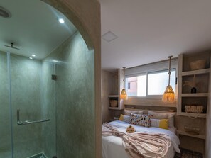 A bedroom with a bed, bedside tables, a window, and a shower area. - Waves Hunter Surf House - Anza (Agadir)