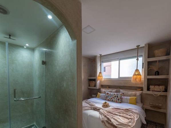 A bedroom with a bed, bedside tables, a window, and a shower area.