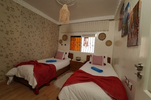 A bedroom with two beds, a window with curtains, a decorative wall hanging, and a door. - Waves Hunter Surf House - Anza (Agadir)
