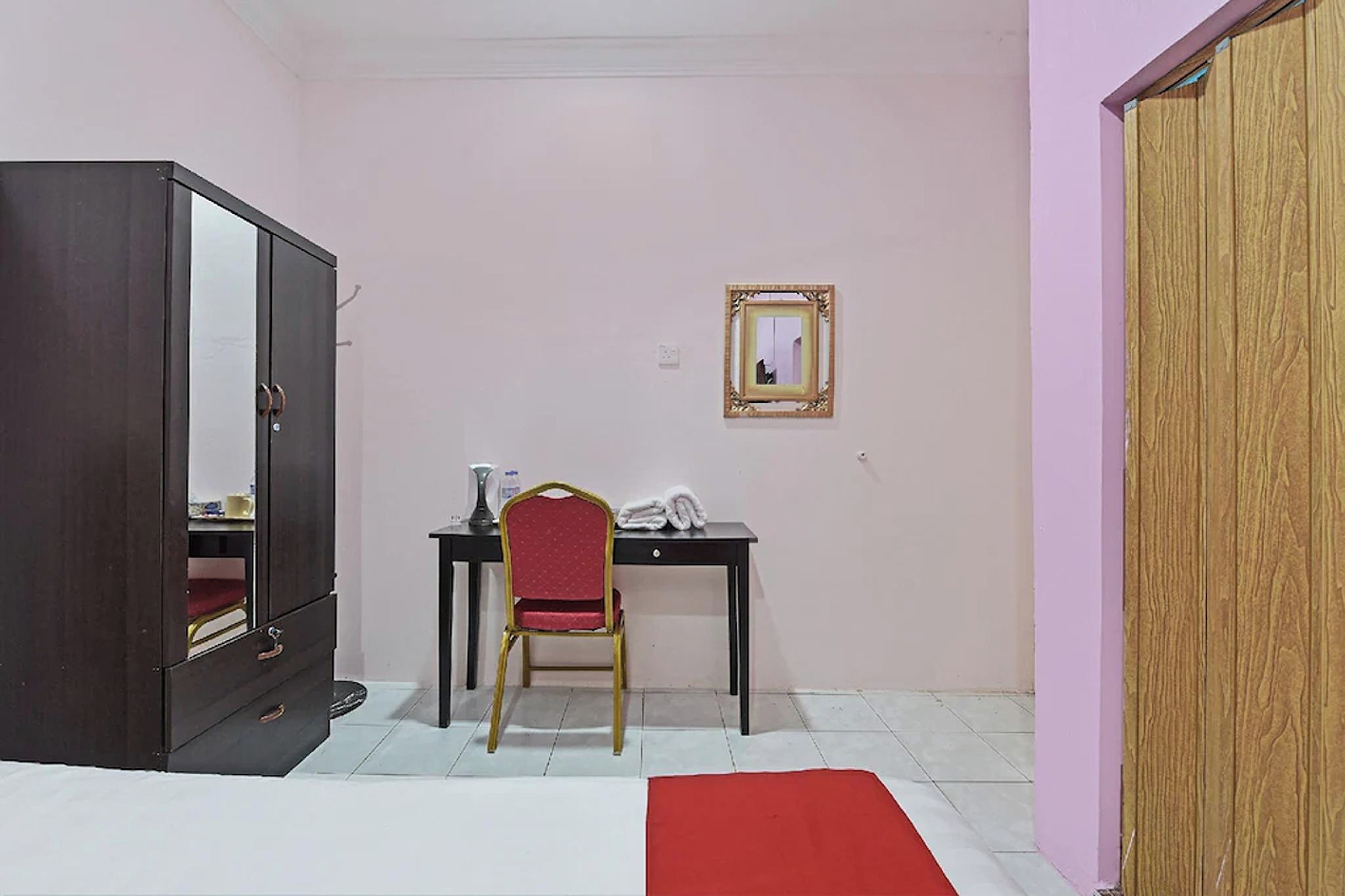 Una habitación con cama, un armario, un escritorio con silla y un espejo en la pared.