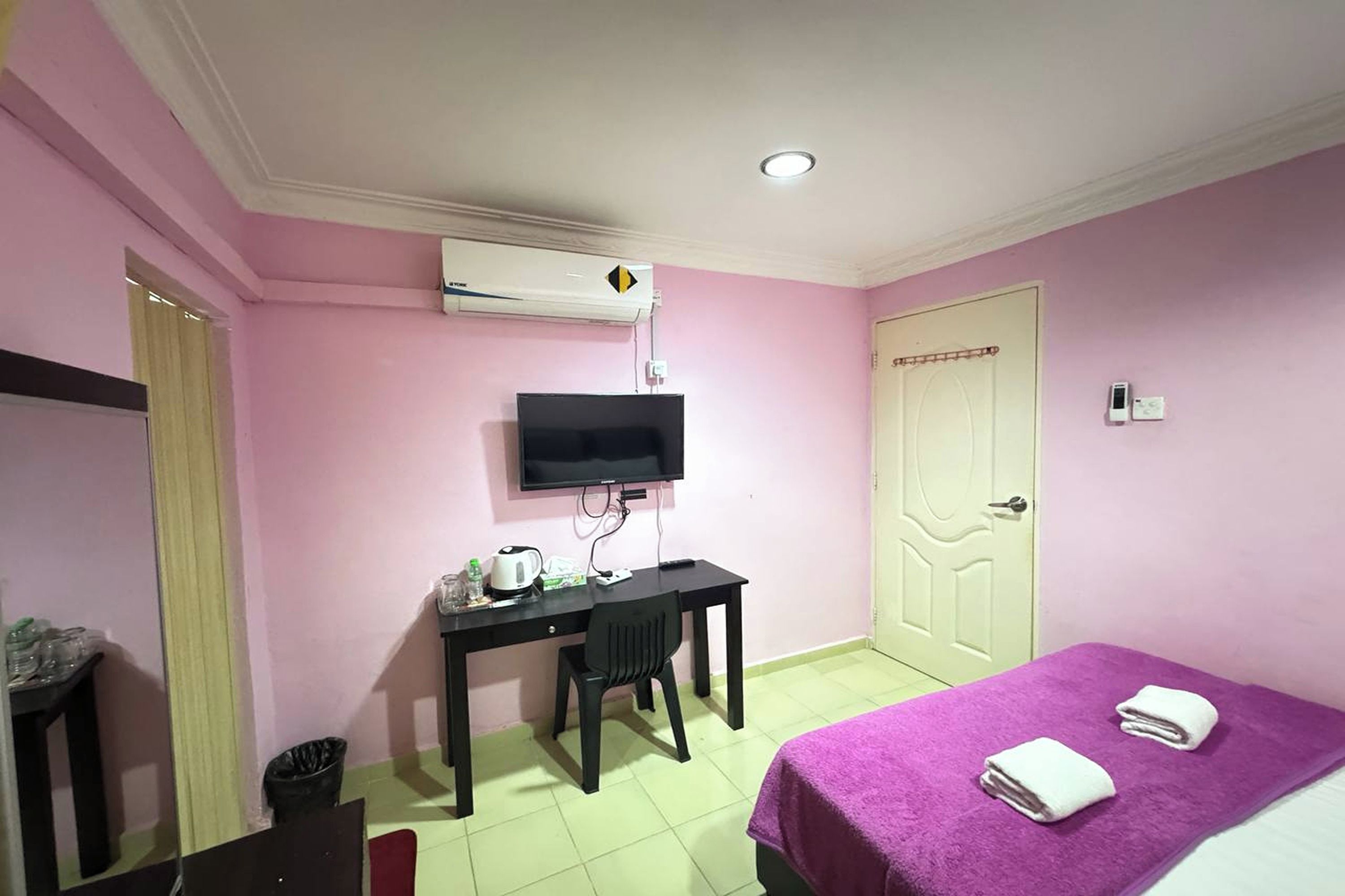 A room with a bed, a desk, a television, and an air conditioning unit.