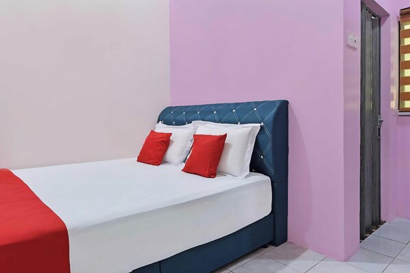 A single-bed room with a white and red bedspread, a blue upholstered headboard, and pink walls.