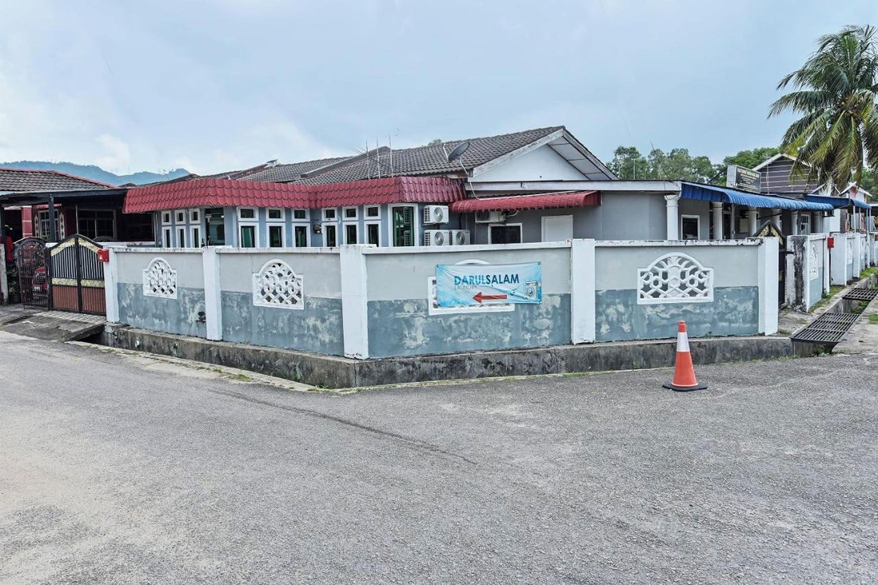 A building with a sign for DarulSalam Laundry, a gated entrance, and a small orange traffic cone.