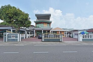 Un edificio de varios pisos con un atrio central, entrada protegida por una reja y zona de estacionamiento.
