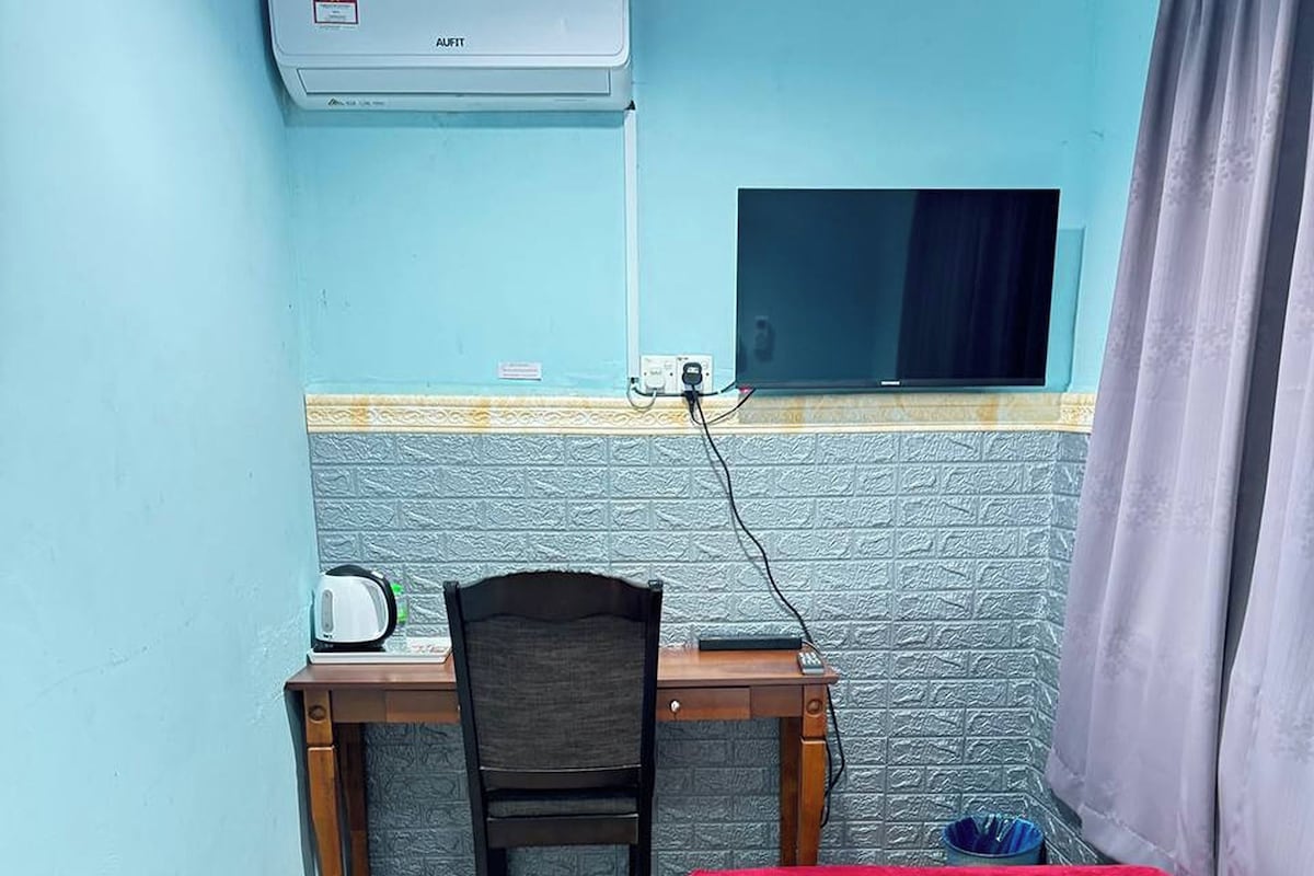 Una habitación pequeña con una cama, un escritorio con silla, aire acondicionado y una ventana con cortinas.