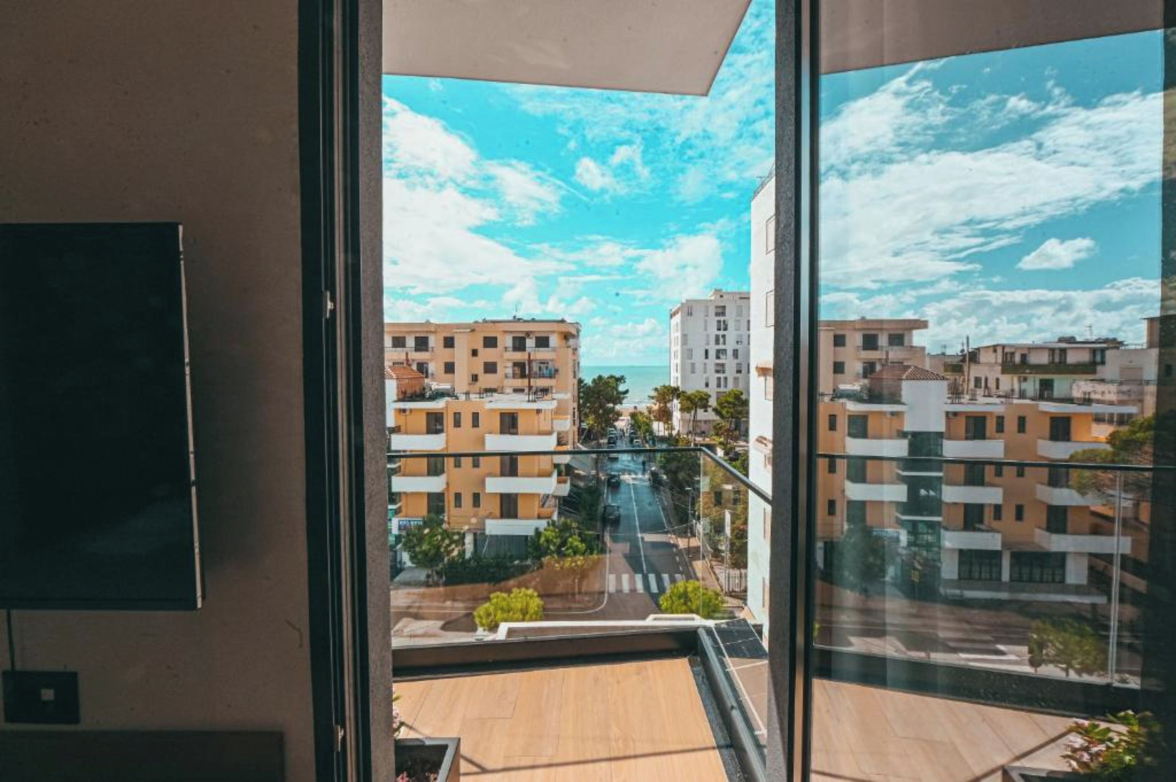 Une vue depuis un balcon, avec un ciel dégagé, donnant sur une rue bordée d’immeubles et d’espaces verts.