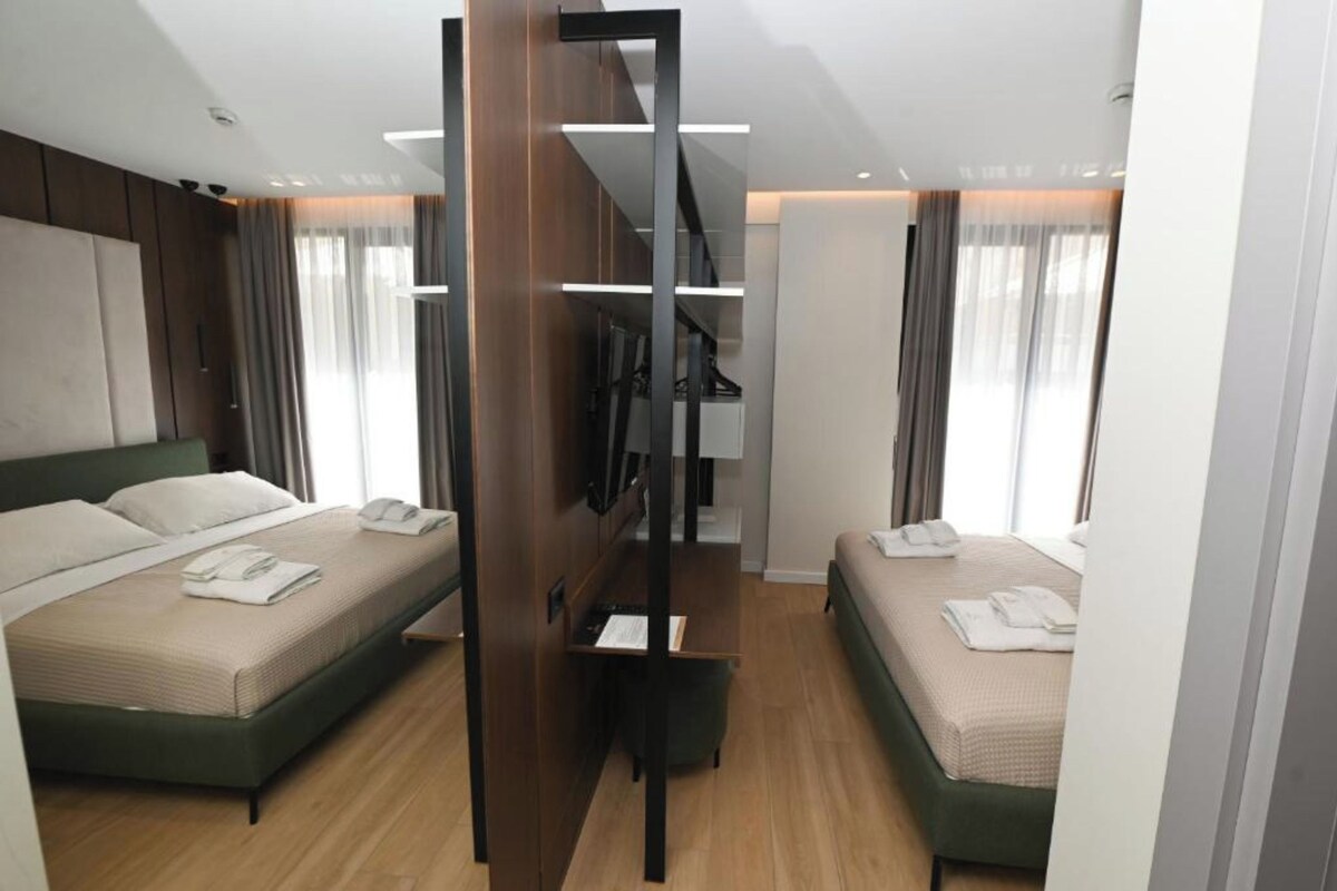 Ein modernes Hotelzimmer mit zwei Betten, einem eingebauten Kleiderschrank und einer kleinen Sitzecke.