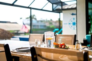 An outdoor dining area with a table set for two, clear glasses, a bottle, and a plate of food. - A Harbour's Walk |Gulf Access |Pool & Spa |Game Room (Cape Coral)