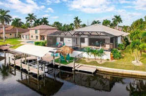 A waterfront property with a pool, a covered outdoor seating area, and a thatched-roof structure. - A Harbour's Walk |Gulf Access |Pool & Spa |Game Room (Cape Coral)