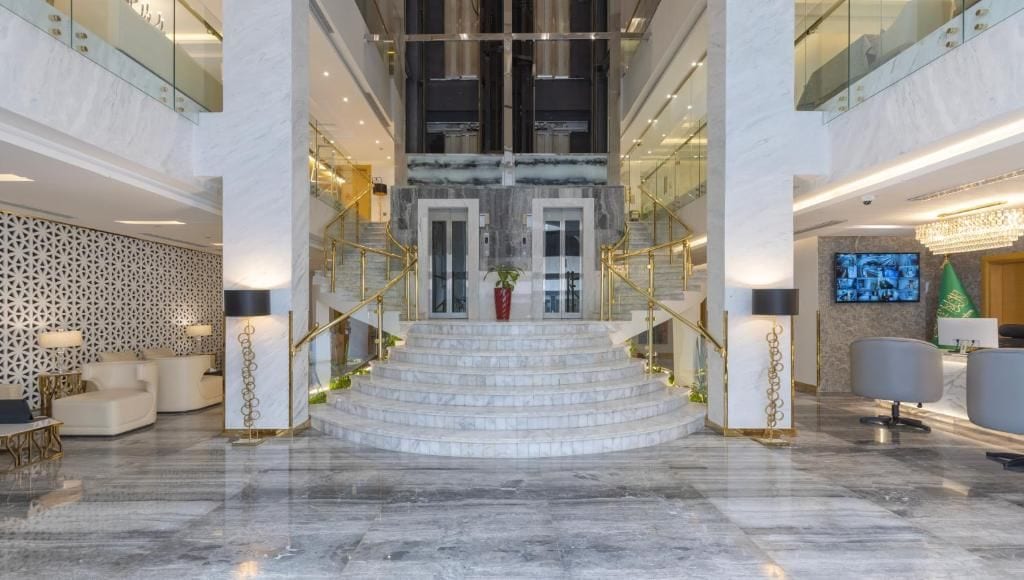 A grand lobby with marble flooring, a central staircase, and modern furnishings.