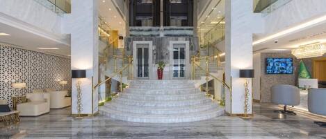 A grand lobby with marble flooring, a central staircase, and modern furnishings.
