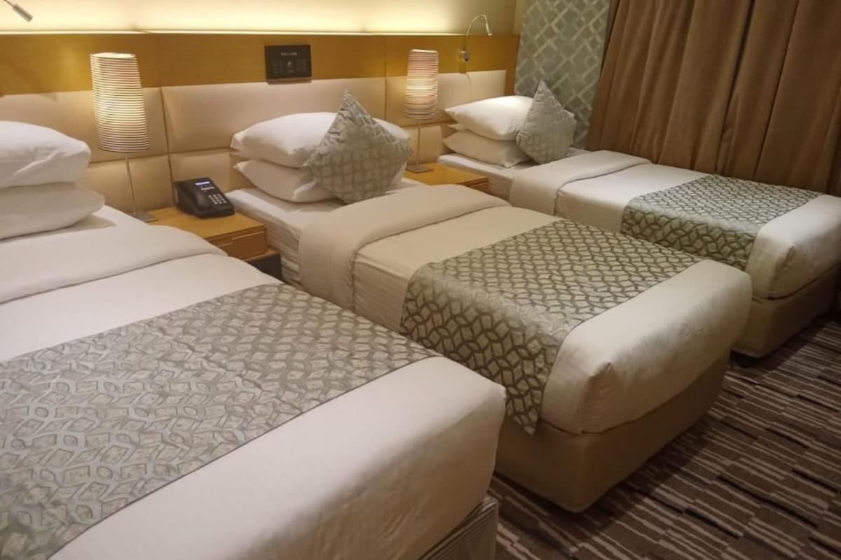 Habitació d'hotel amb tres llits, cada un amb un llençol estampat, vàries làmpades de nit i un telèfon a la meseta.