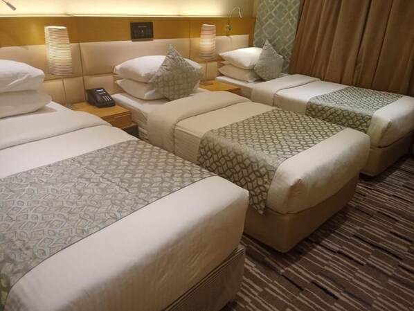 Quarto de hotel com três camas, cada uma com colcha estampada, luminárias e telefone.