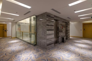Um saguão de hotel com uma recepção de mármore, paredes de vidro e um carpete estampado.