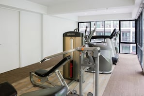 Ein Fitnessstudio mit Cardiogeräten, Krafttrainingsgeräten und einem großen Fenster mit Blick auf Gebäude.
