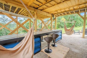 Ett utomhusområde med sittplatser under tak, bestående av ett bord och stolar, en hängmatta och utsikt över den omgivande grönskan.