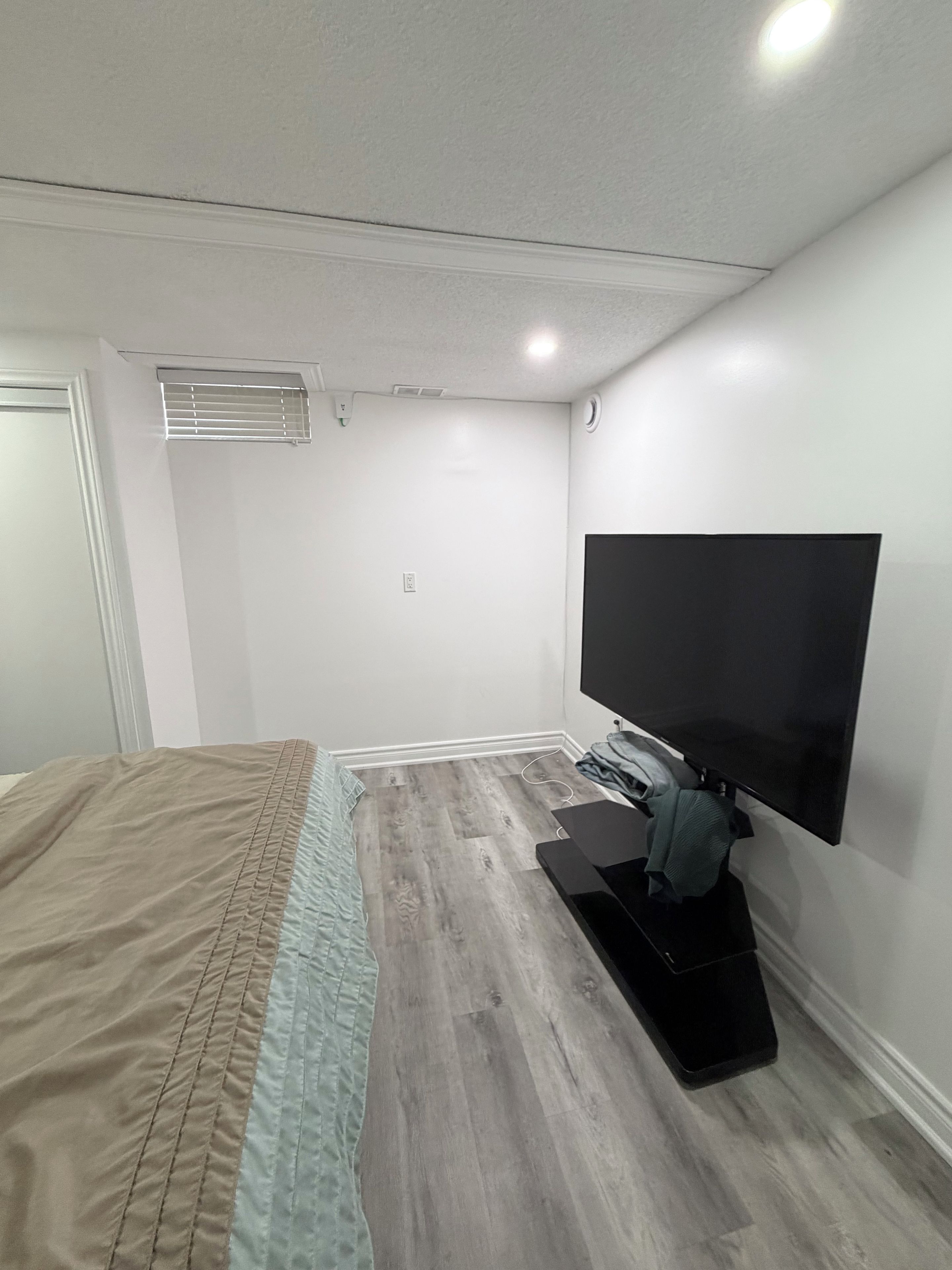 A bedroom with a bed, a flat-screen TV mounted on the wall, and a small desk with a chair.