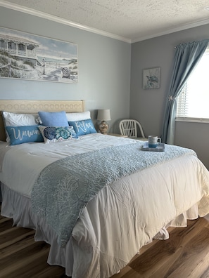 Een slaapkamer met een bed, een schilderij, een stoel, een raam met gordijnen en een lamp.