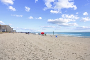 A wide sandy beach with a clear sky, a few umbrellas, and beach chairs. - Chateau By The Sea-Oceanfront-Sleeps4-2b/2b-Laundry-Kitchen-Pool-Free Parking (North Myrtle Beach)