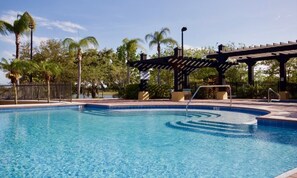 Ein Schwimmbecken mit einer Holzpergola und Palmen im Hintergrund.