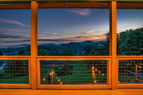 Un balcón con vistas a un atardecer sobre un paisaje con árboles y colinas.