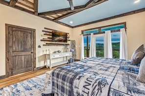 Un dormitorio con una cama grande, una puerta de madera, un tocador blanco y una ventana con cortinas.