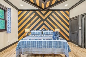 A bedroom with a chevron-patterned wall, a bed with a blue and white checkered bedspread, two bedside lamps, and a window with a curtain. - Mountain View, Pool, Pickleball, Golf & Theater (Sevierville)