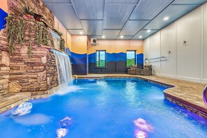 Una piscina interior con una cascada, paredes de piedra y un mural de montañas.
