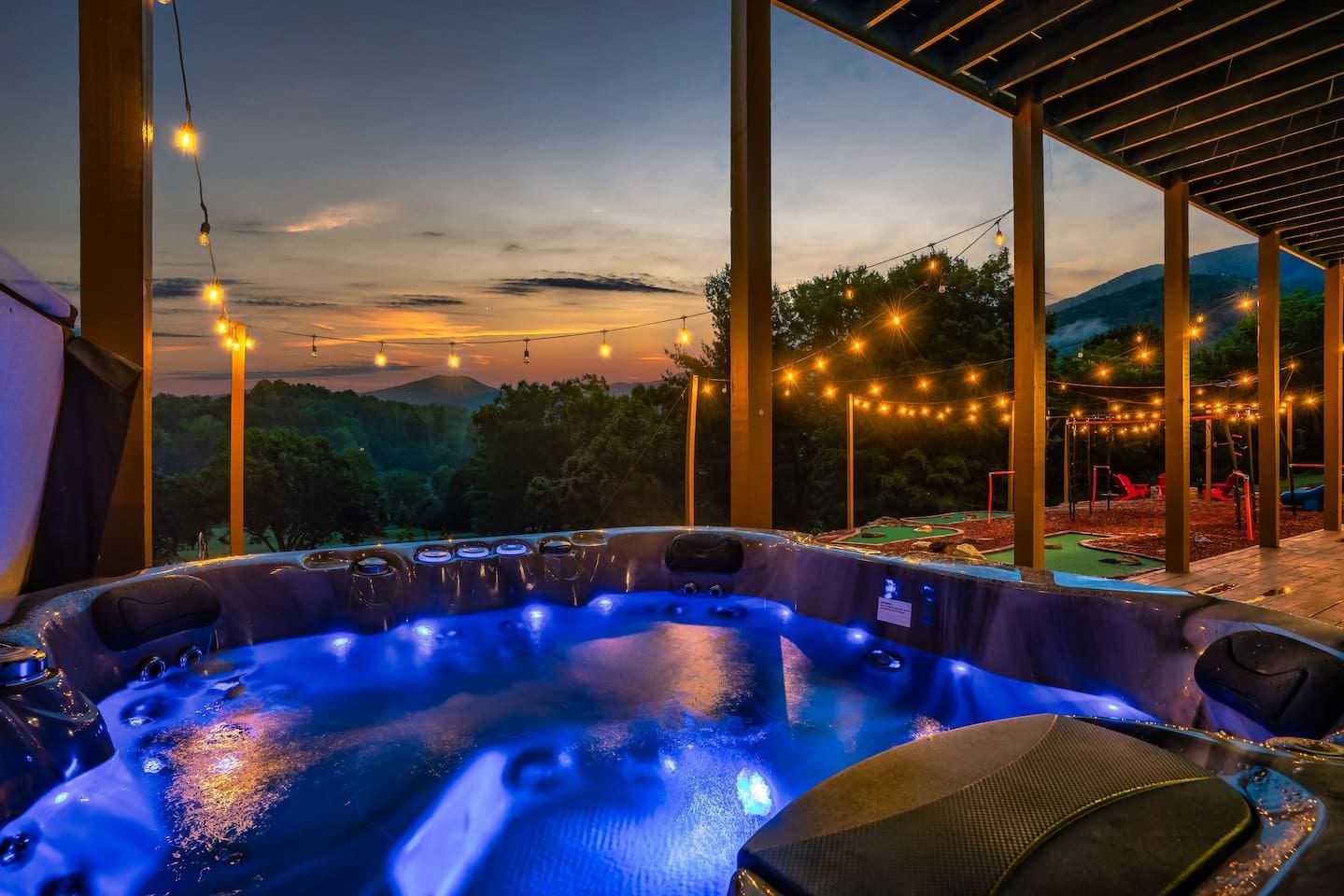 A hot tub area with a view of a mountainous landscape, string lights, and outdoor seating.