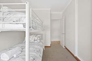 Ein Schlafraum mit Etagenbetten, Teppichboden und einer Tür zu einem weiteren Zimmer.