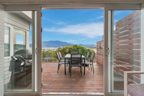 Eine Glastür öffnet sich zu einer Terrasse mit Tisch und Stühlen, mit Blick auf eine malerische Landschaft mit Bergen.