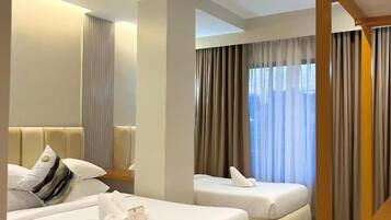 A hotel room with two beds, a sitting area, and a view of the outdoors.